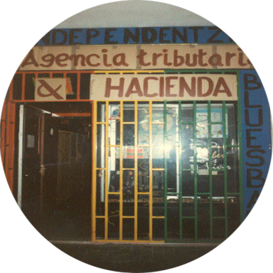 Entrada de una agencia tributaria con rejas de colores y letreros en español.