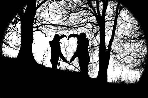 Siluetas de dos personas formando un corazón en un paisaje boscoso.
