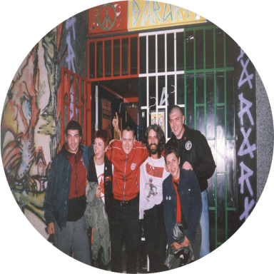 Grupo de seis personas sonriendo frente a una entrada decorada con graffiti.